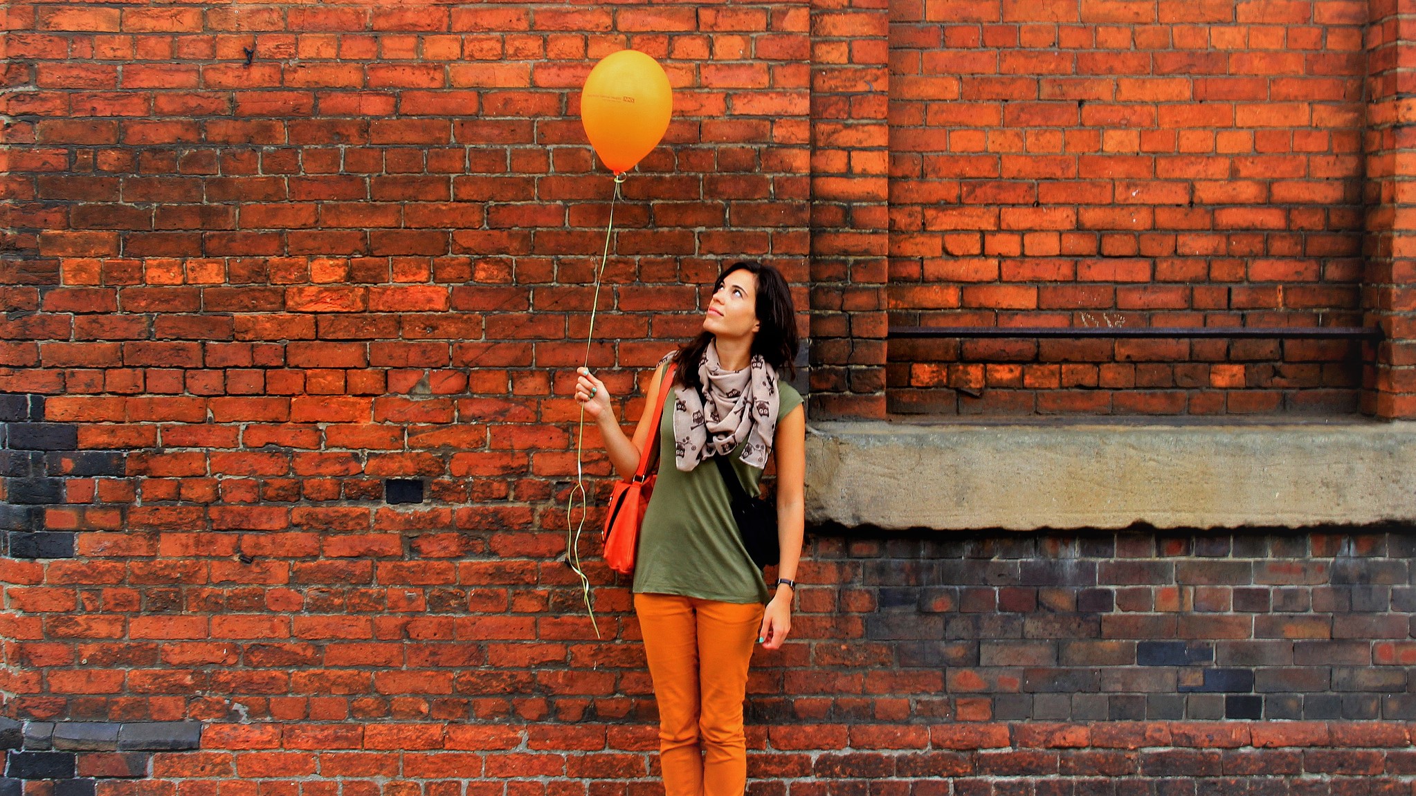 Een jonge vrouw staat voor een muur en kijkt naar een ballon, die ze aan een touwtje vast heeft. Ze ziet er verlegen en rustig uit; niet als een durfal.