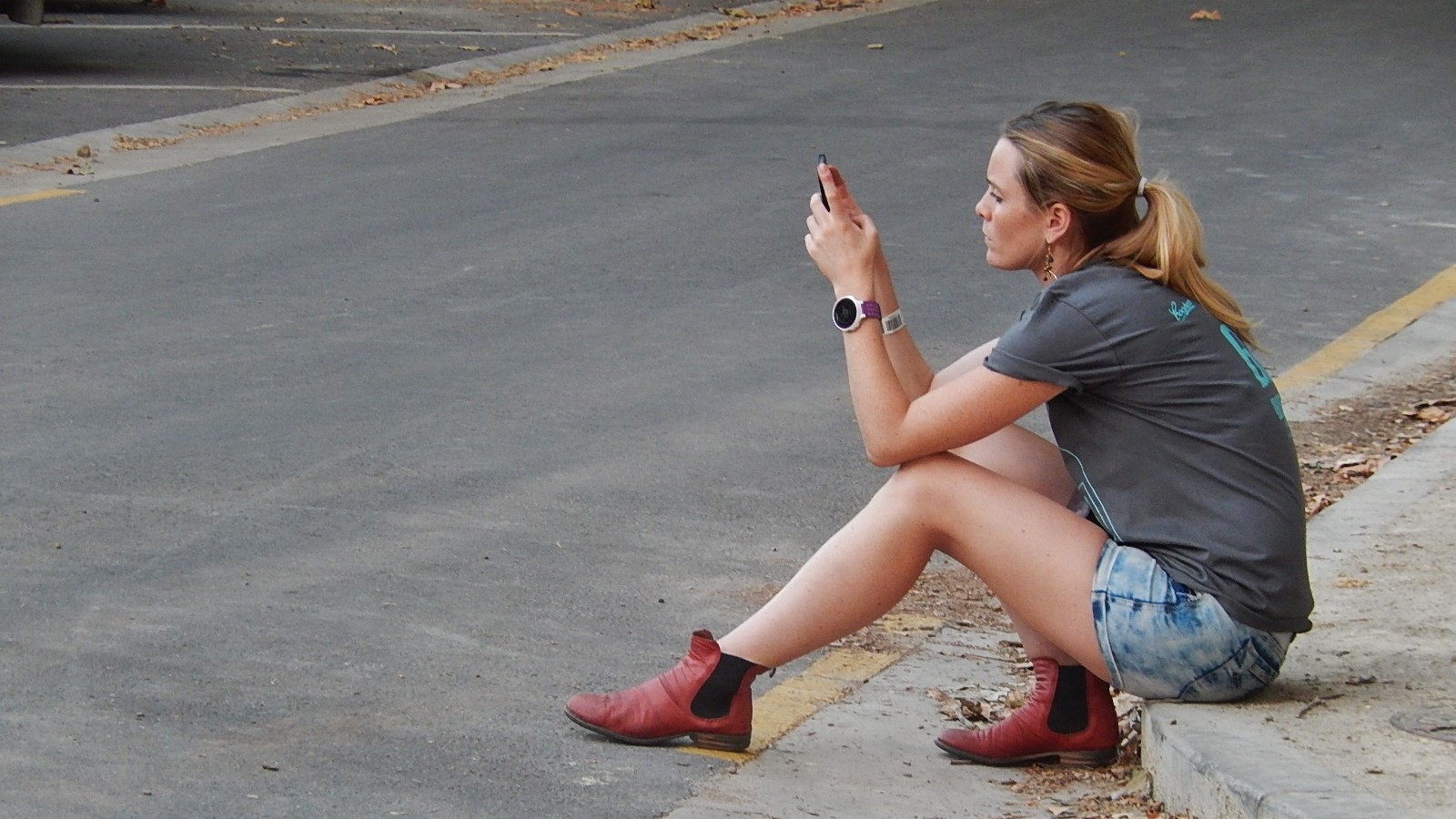 Een jonge vrouw zit op de stoep en kijkt naar haar smartphone.