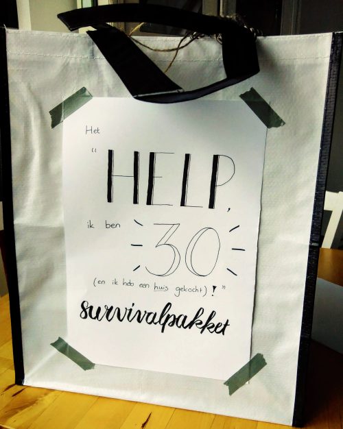 een tas met daarop de tekst "Het "Help, ik ben 30 (en ik heb een huis gekocht)!" survivalpakket"