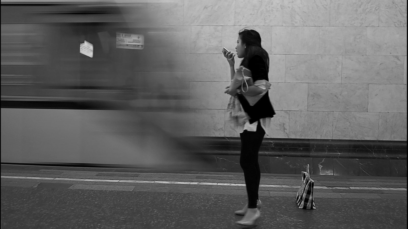een vrouw wacht in haar eentje op de metro, met een smartphone in haar hand