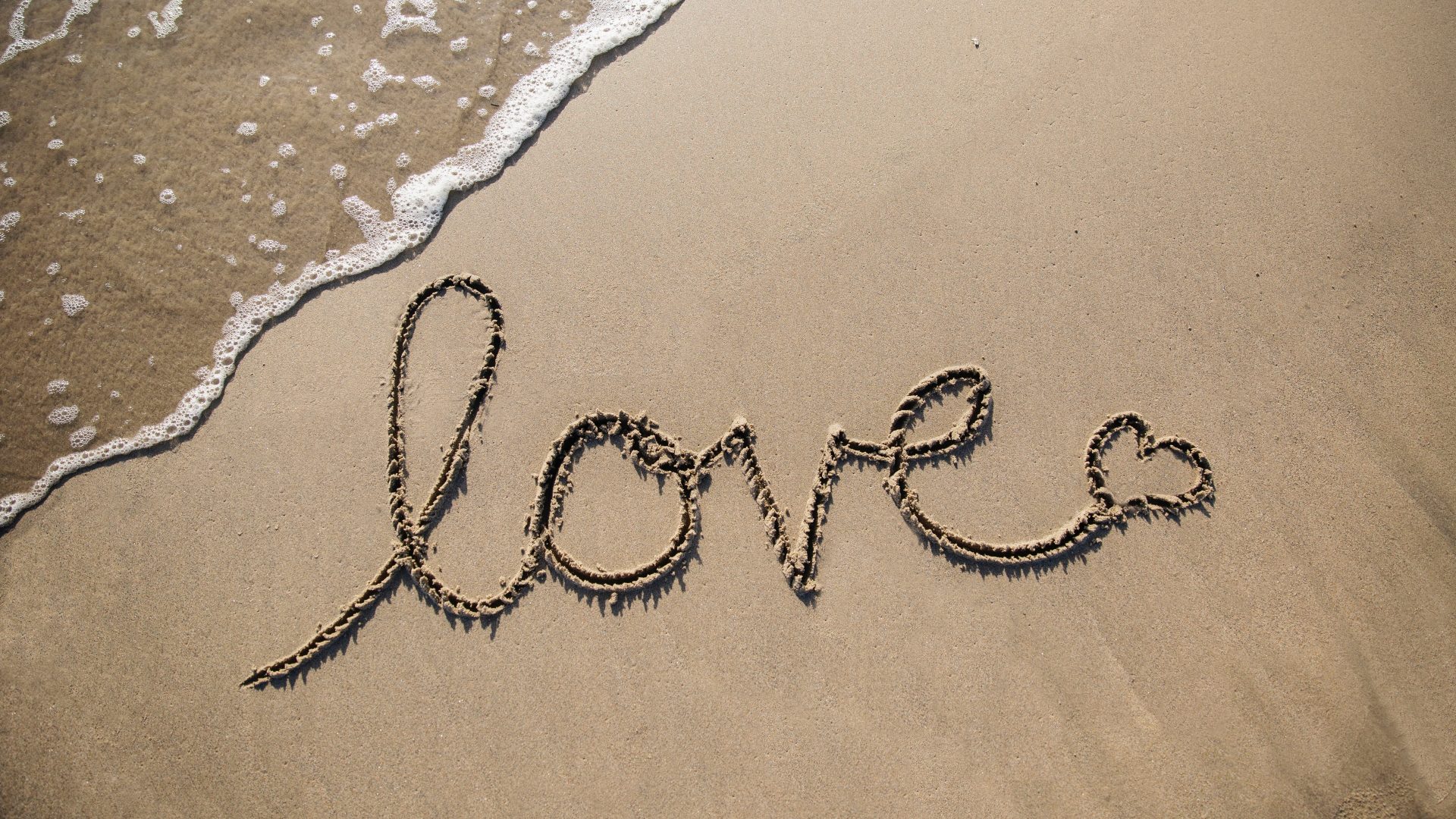 Het woord 'love' staat op het strand geschreven. Zeewater spoelt het bijna weg.