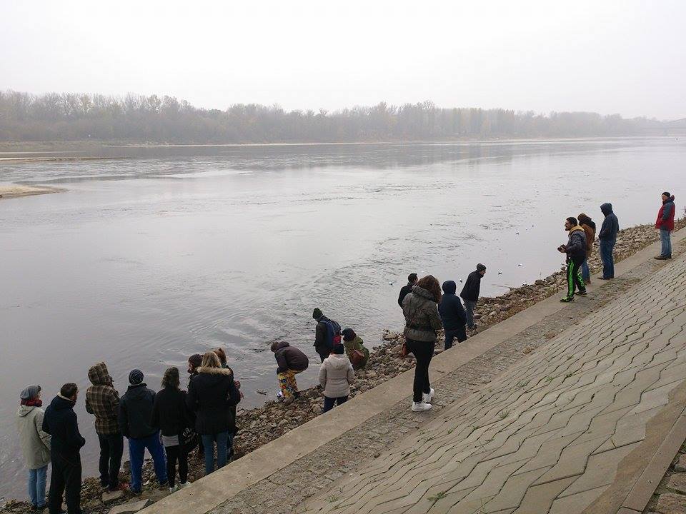 een groep jongeren laat de door hen gevouwen bootjes meevoeren door de rivier